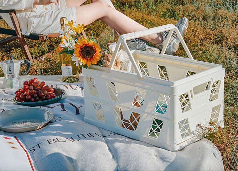 White crate filled with flowers and wine, displayed on a picnic mat