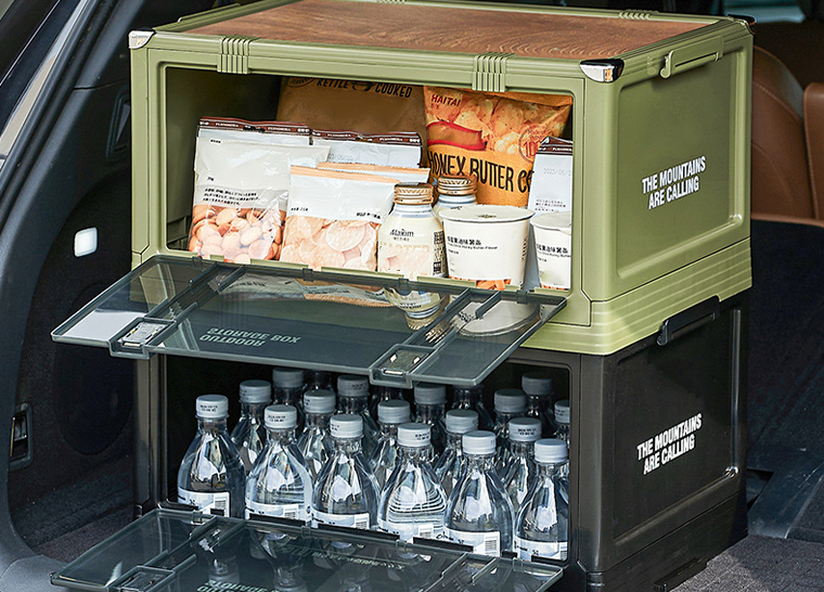 Two stacked outdoor storage boxes in a car trunk, filled with snacks and drinks.