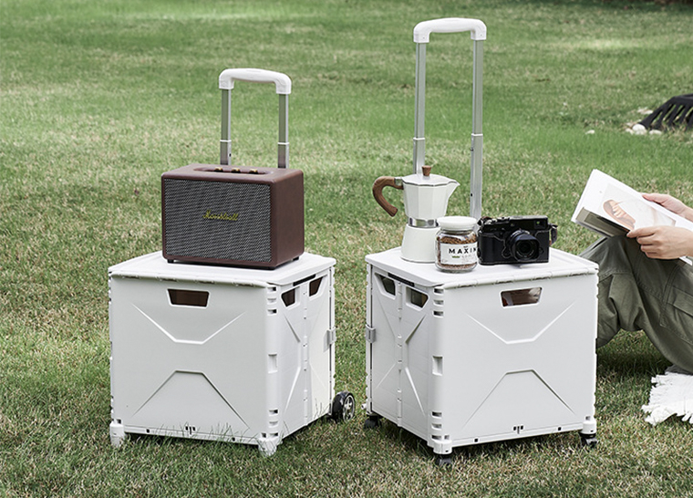 Two foldable storage boxes used as outdoor tables with speaker, moka pot, camera and coffee