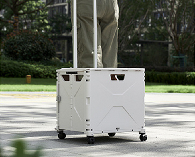 Person standing on a foldable rolling storage box with telescopic handle outdoors