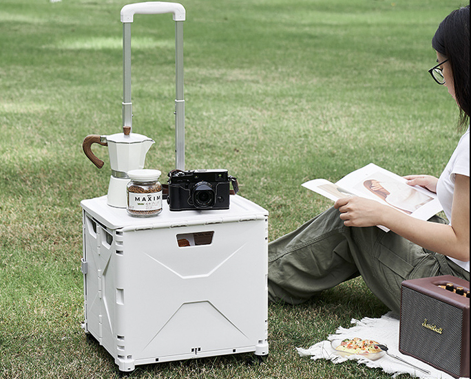 Foldable storage box used as a side table during outdoor leisure with camera, coffee and book
