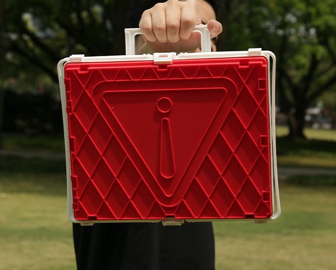Person holding a red foldable storage box with emergency warning icon outdoors