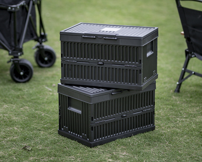 Two black foldable storage boxes stacked outdoors on grass