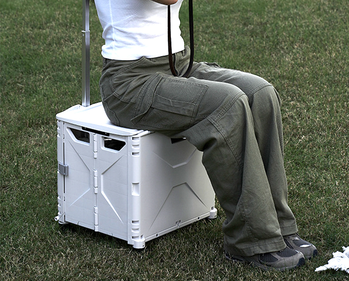 Person sitting on a foldable storage box with wheels on the grass