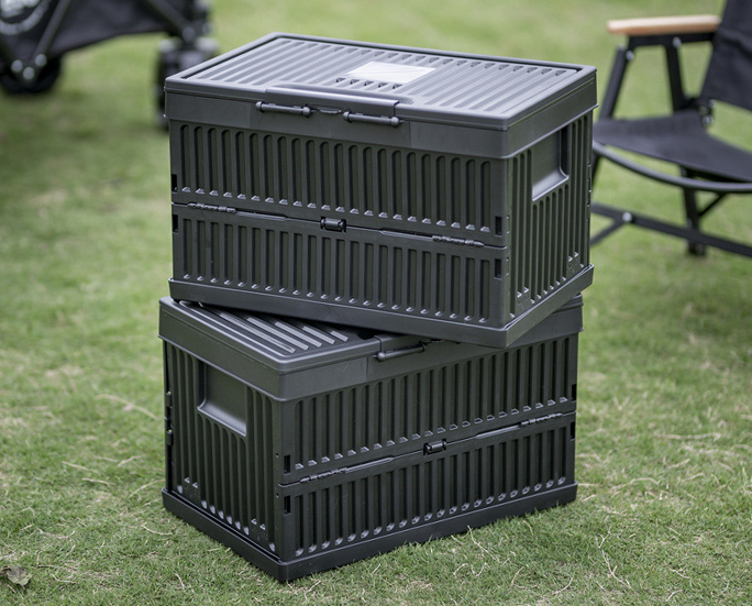 Two black collapsible storage containers crisscross stacked on grass