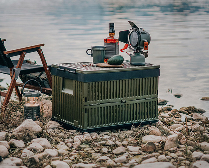 Military green outdoor storage box with drinks and lantern beside lake