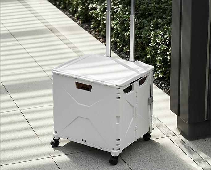 Foldable storage box with wheels and telescopic handle placed outdoors on pavement