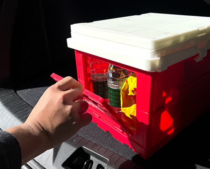 Hand opening the side door of a red foldable storage box in a vehicle
