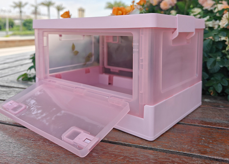 Outdoor photo of pink folding storage box with front door open on wooden table