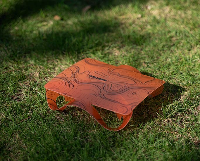 Mesa de camping plegable con estampado topográfico naranja sobre césped