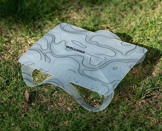 Mesa de camping plegable topográfica blanca colocada sobre césped.