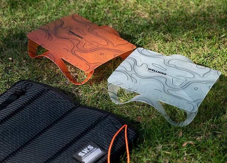 Mesa de camping plegable en color naranja y gris claro sobre césped.