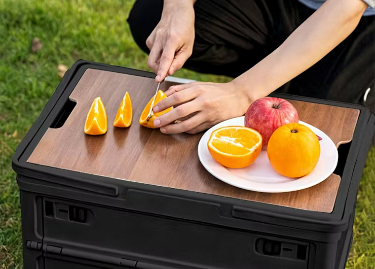 Foldable camping storage box with wooden lid used as outdoor cutting table
